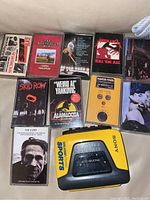 Sony Walkman WM-AF33 Sports cassette player in yellow and black with 10 assorted music cassette tapes from various artists including Metallica, Weird Al Yankovic, Skid Row, and The Cure.