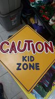 Front side of yellow diamond-shaped plastic sign with the text 'CAUTION KID ZONE'.