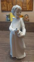 Front view of the white porcelain Nao Lladro angel figurine showing the figure with hands together holding an item, head slightly bowed.