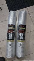 Photo showing two new aluminum flexible duct pipes in packaging, with labels visible.