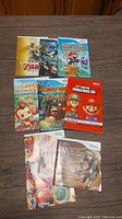 Top-down image showing all 8 Nintendo Wii game manuals arranged on a wooden surface with visible titles and cover artwork including Zelda, Donkey Kong, Mario Party, and others.