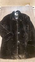 Front angle showing black faux fur coat laid flat with textured pattern and button closure