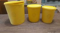 Front view of three vintage yellow Tupperware containers with embossed sunflower design.