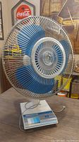 Front view of vintage wired oscillating fan showing blue blades and wire cage