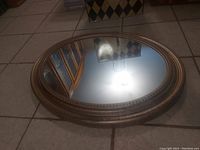 Front view of the oval mirror showing reflective glass and decorative textured plastic frame.