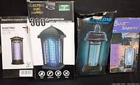 Four electric bug zappers in original factory packaging with brand names and images visible on boxes.
