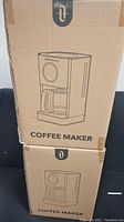 Two sealed TaoTronics coffee makers in original cardboard boxes stacked vertically on a black surface.
