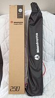 Manfrotto Imagine More 290 tripod original cardboard box next to the black carrying bag with white Manfrotto logo.