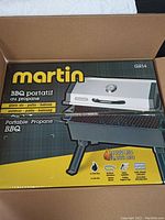 Photo of the boxed Martin portable propane BBQ showing branding, model GR14, and 14000 BTU power output, highlighting patio and balcony suitability.