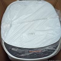 Top view of portable mini washing machine with control panel covered in plastic in box