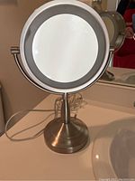 Round lighted vanity mirror on bathroom counter showing brushed metal finish and white illumination