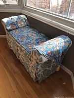 Upholstered window seat bench positioned next to windows, featuring decorative runner with blue, beige, and red patterns over blue and white floral upholstery.