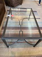 Rectangular coffee table with glass top and black metal frame, front view on striped carpet