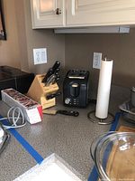 Wusthof knife block with seven knives and scissors, black Sunbeam 2-slice toaster, paper towel holder, and part of the Miracle Whisk packaging on countertop.