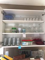 Glass cabinet shelves showing a variety of clear glass wine glasses and plastic food storage containers with lids.