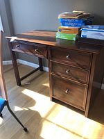 Front view of the wooden office desk with three drawers and keyboard slide, showing paper items on top and silver knobs on drawers