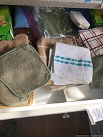 First photo showing an open kitchen drawer containing assorted linen items such as dishcloths and towels in multiple colors and textures, some folded and others stacked.