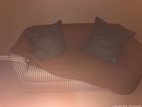 Image of striped fabric loveseat with brown cover and two cushions in a basement setting.