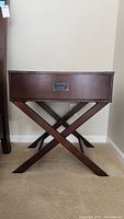 Front view of wooden nightstand with one drawer and crossed leg base against wall