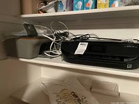 Shelf with two HP printers and associated cables and accessories.