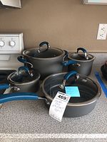 Full set of four pots with glass lids and blue silicone handles arranged on a countertop near stove