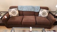 Full frontal photo of the brown sofa with blue throw blanket and two decorative pillows, showing the overall style and condition.