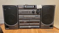 Front view of AIWA stereo system with two speakers, showing cassette deck, tuner, and control buttons.
