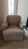 Front view of a fabric upholstered swivel armchair rocker with padded arms and skirted base.
