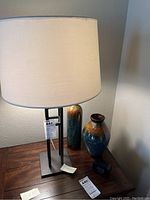 Metal table lamp with white shade and two ceramic vases on a wooden surface