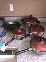 Four lidded Wear Ever pots and one Calphalon skillet on countertop.