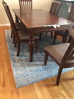 Full dining table with six chairs placed on the turquoise and cream patterned Pier 1 rug.