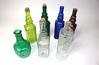 Overview of 7 colored decorative glass bottles in various shapes with cork stoppers