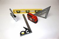 Photo of all measuring tools arranged on white surface showing the variety of items including spirit level, tape measures, set squares, and combination square