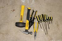Full view showing the lump hammer, claw hammer, needle nose pliers, standard pliers, tin snip, and screwdrivers laid out on the floor