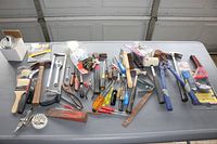 Various household tools laid out showing items including hammers, paint brushes, pliers, wrenches, scrapers, and bolt cutters