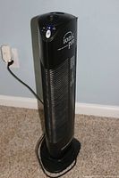 Full view of black Ionic Pro air purifier standing on carpeted floor, plugged into wall outlet.