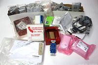 View of large lot with steel outlet plates, light switches, motion sensors, some items still in boxes and sealed plastic bags