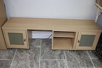 Front view of long maple color TV stand with two smoked glass door cabinets and center open shelf.