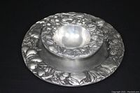 Angle view of 8" pewter bowl with raised fruit pattern forming an outer ring, smooth inner surface, matching platter below.