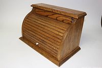 Front view of vintage wooden bread bin showing curved roll-top door and white knob handle