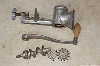 Top view photo showing metal body of Universal 2 food grinder with clamp, wooden handle, grinding screw, and 3 circular cutting blades.