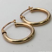 Close-up image of the pair of small yellow gold hoop earrings showing polished surfaces and snap closure.