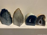 Four quartz agate geodes in a row on a white surface against a plain wall showing color and size differences