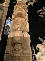 Full length view of the large carved wooden totem laid on black carpet with water bottle for scale