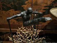 Side view showing male figure's pose and detailed texture, displaying extended limbs and balance on thin rods.