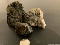 Photo showing three natural rock geodes in varying sizes placed on dark surface with a quarter for scale. Geodes have rough irregular outer surfaces in shades of brown and gray.