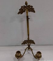 Full view of vintage brass wall sconce with two candle cups and ornate oak leaf decoration at base and top acorn finial.