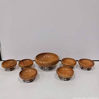 Full set of seven wooden and chrome pedestal salad bowls displayed on white surface.