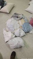 Two large white pillows and several wrapped bedding items in various muted colors placed on the floor.
