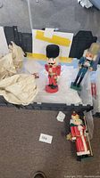 Three nutcracker figurines placed in and around a plastic case, showing different styles and uniforms.
